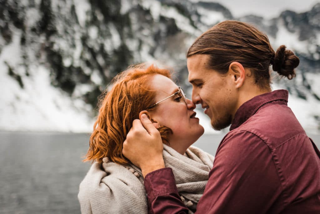 couple touching noses in front of lake and mountains