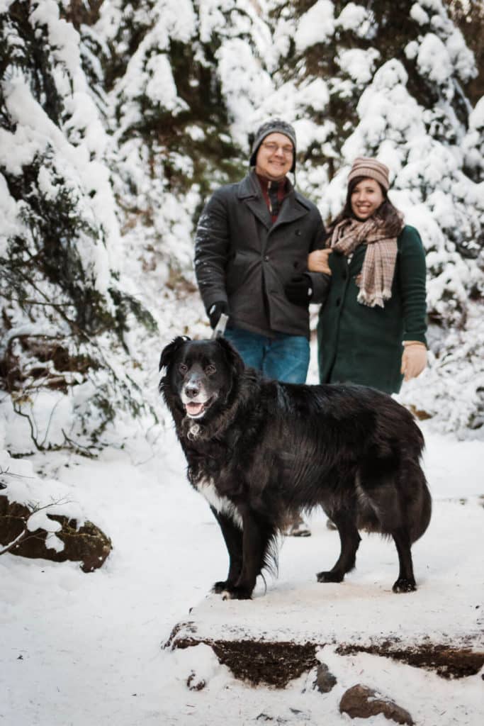 couple standing with dog on snow covered trail