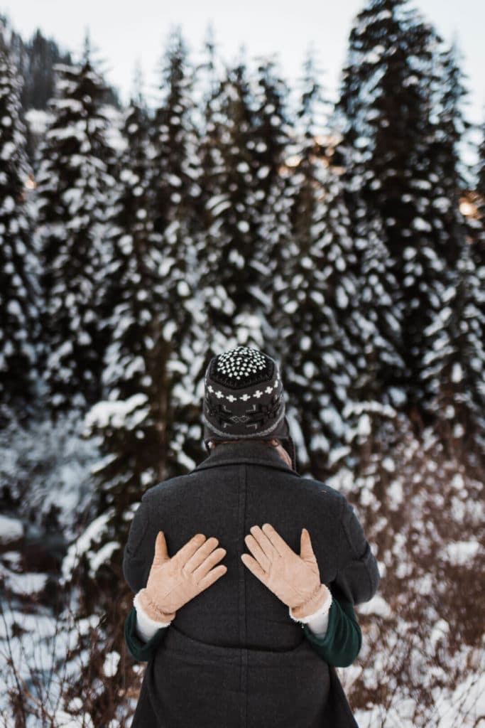 couple hugging in snow in front of trees