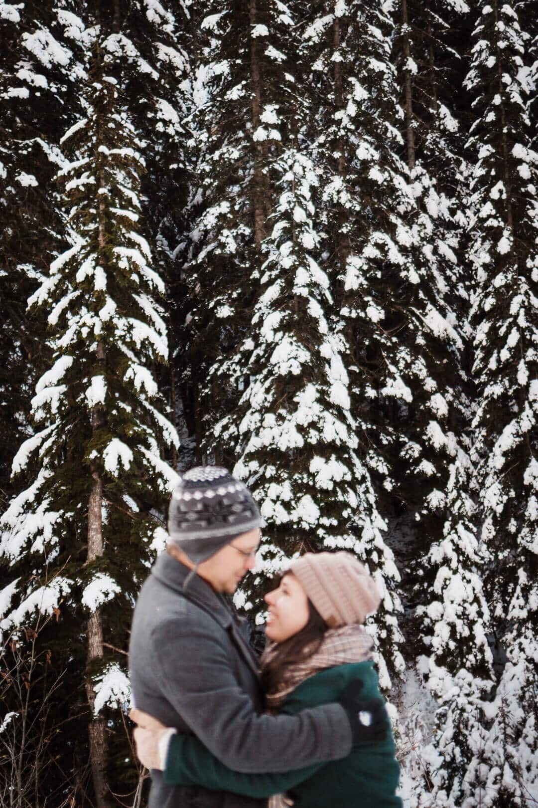couple hugging in snow in front of trees