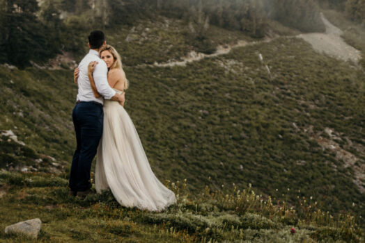 bride and groom hugging in mountain meadow with mountain in background