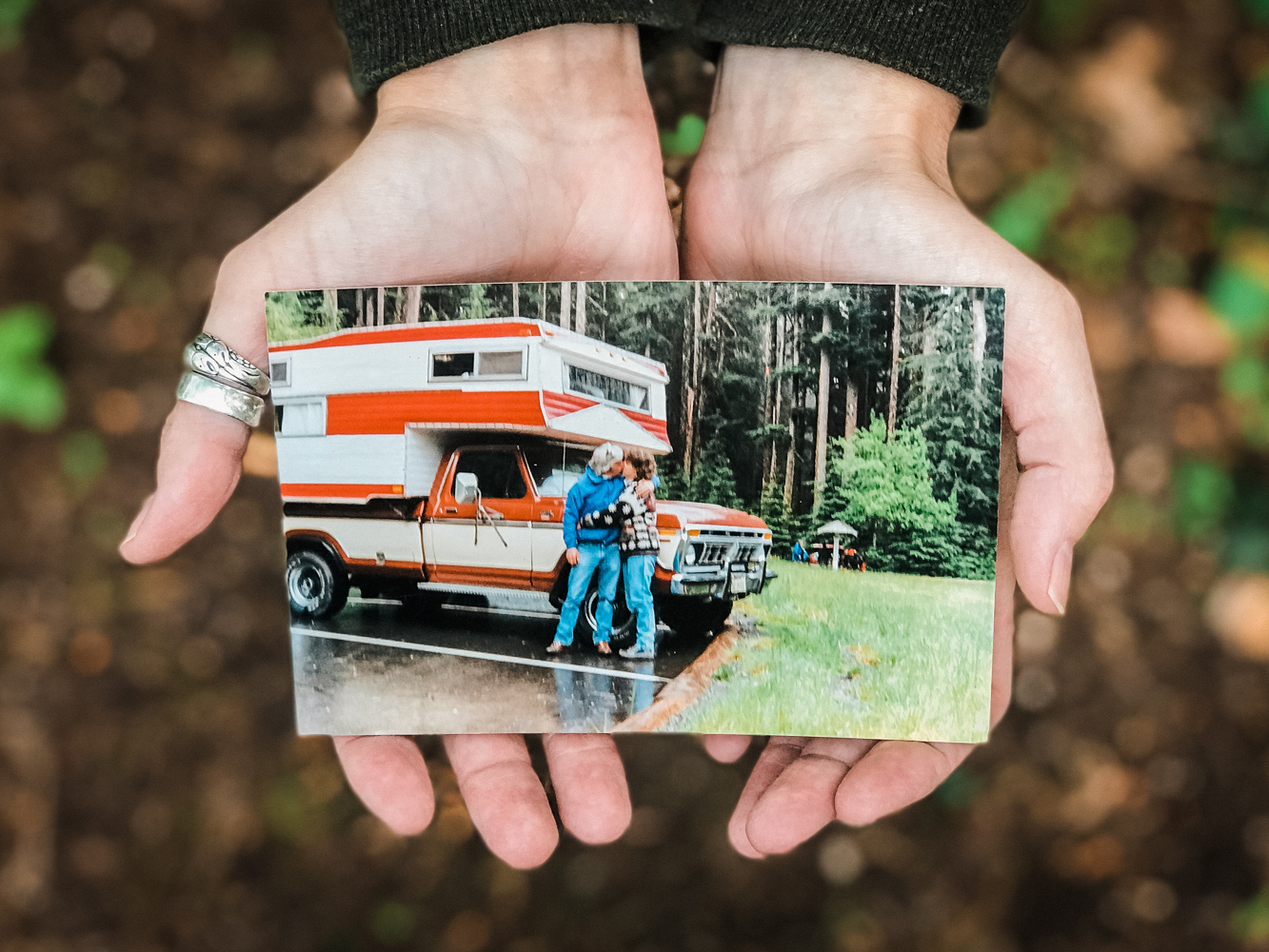 photo of hands holding photo of couple kissing in front of red and white camper