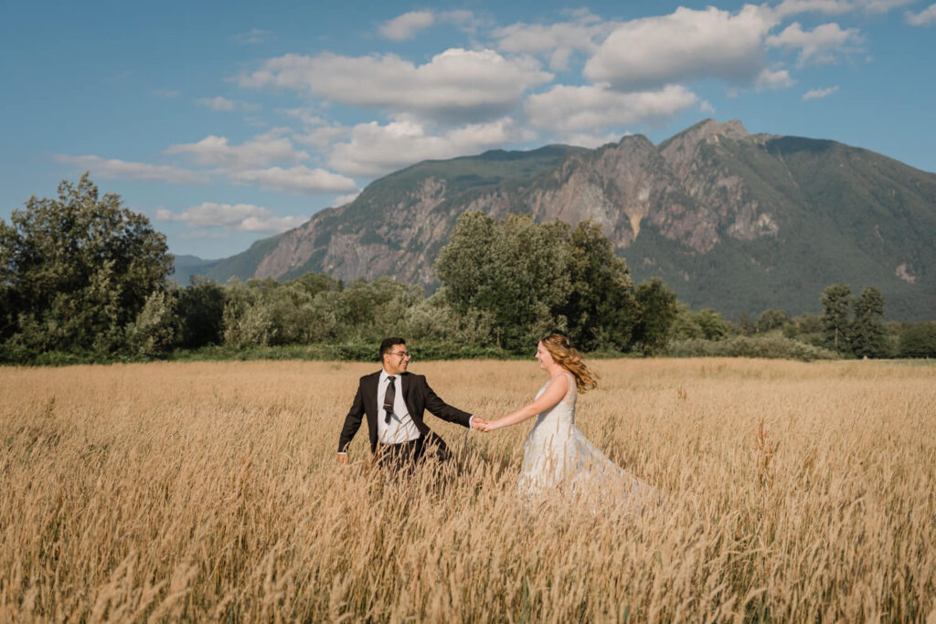A couple runs through a field of grass in front of a mountain