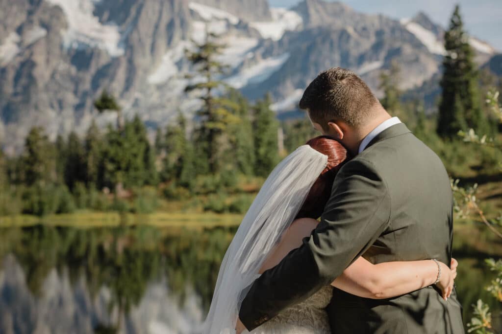 two people hug beside a lake while looking at a mountain
