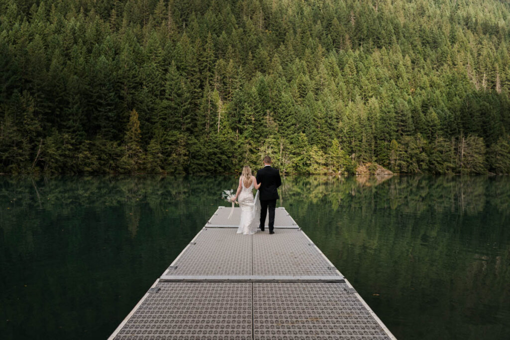 two people walk out onto a dock on a lake with trees in the background